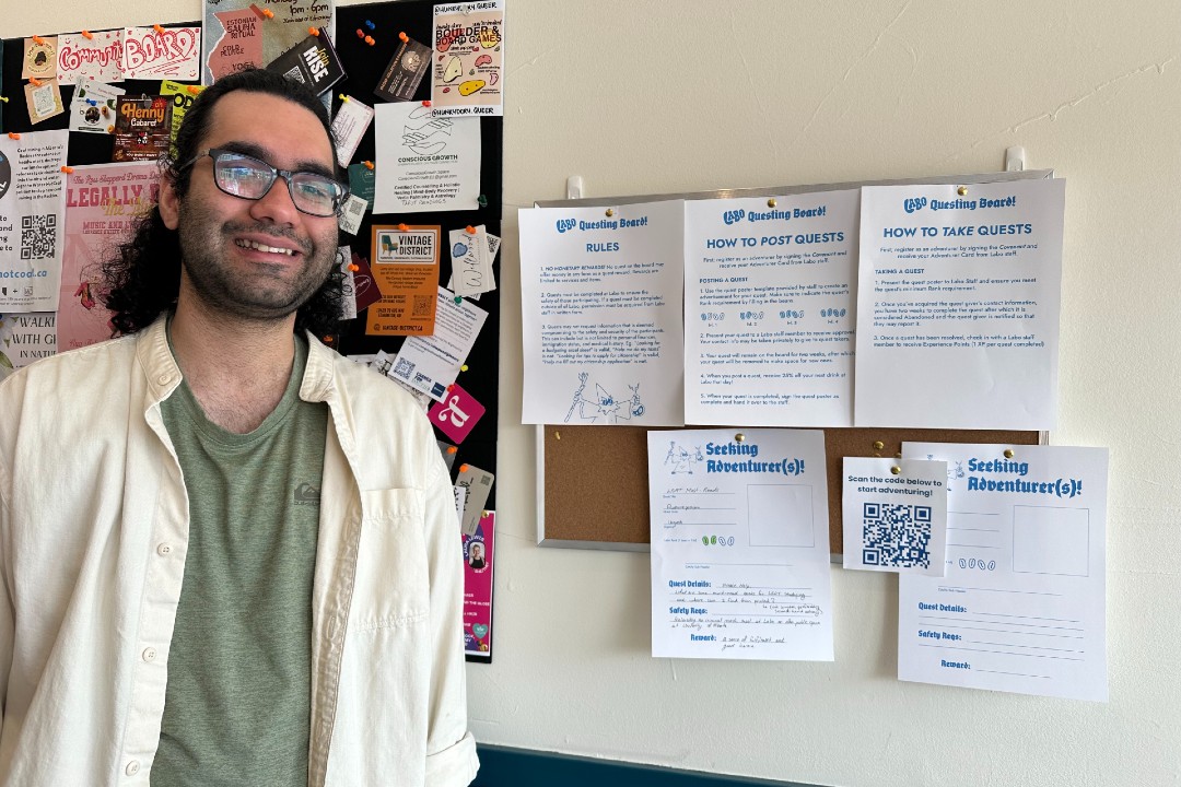 A man stands in front of a bulletin board with white and blue papers pinned to it.