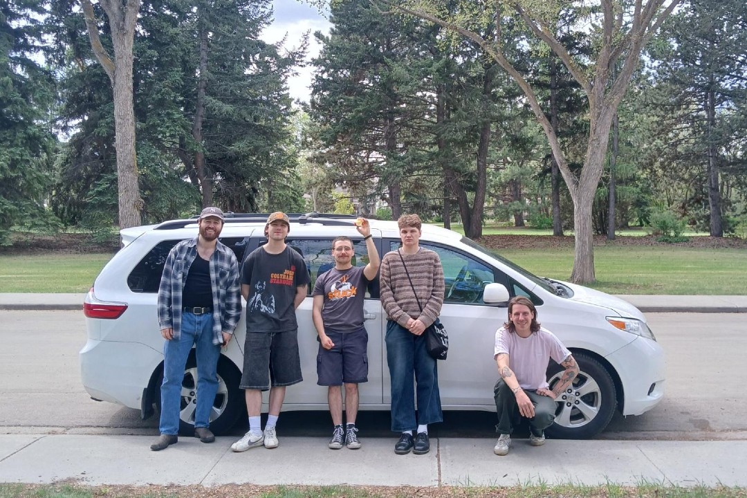 Five people pose in front of a van on a tree-lined street