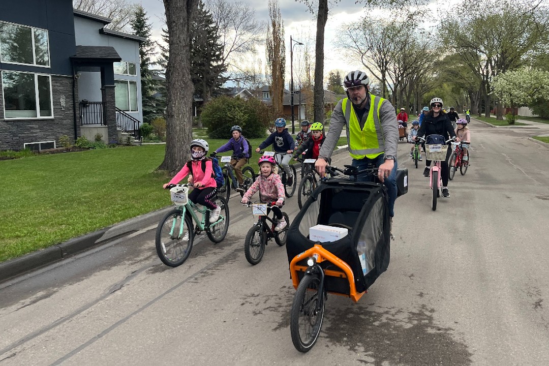 A group of children and adults ride bikes down a residential road