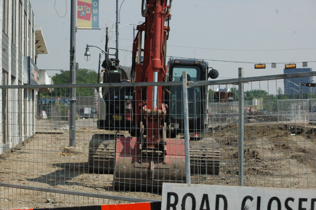 A large piece of construction equipment behind a fence and a Road Closed sign