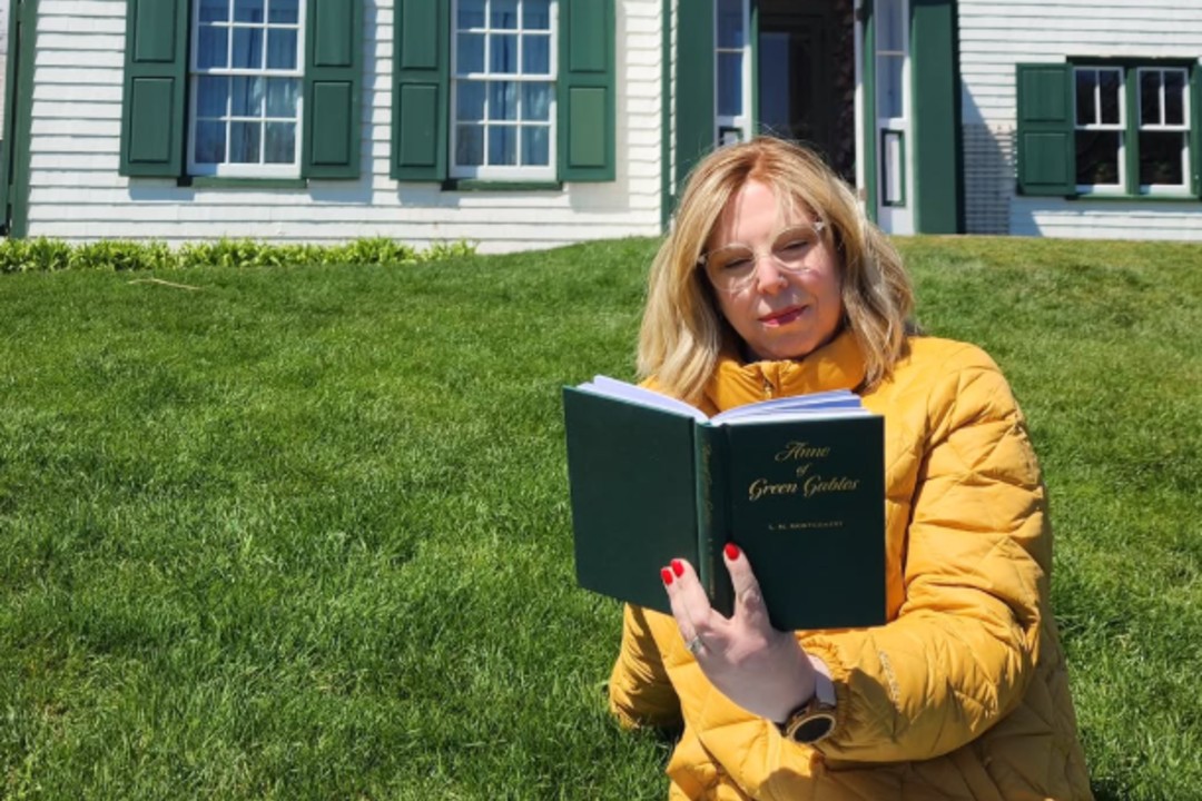 A woman sitting in front of a white house reading a book