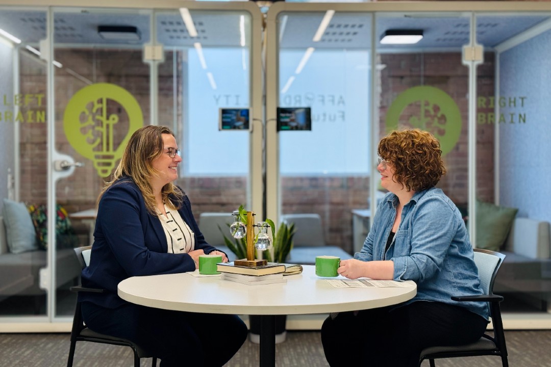 Two people seated across a table from one another in a workspace.