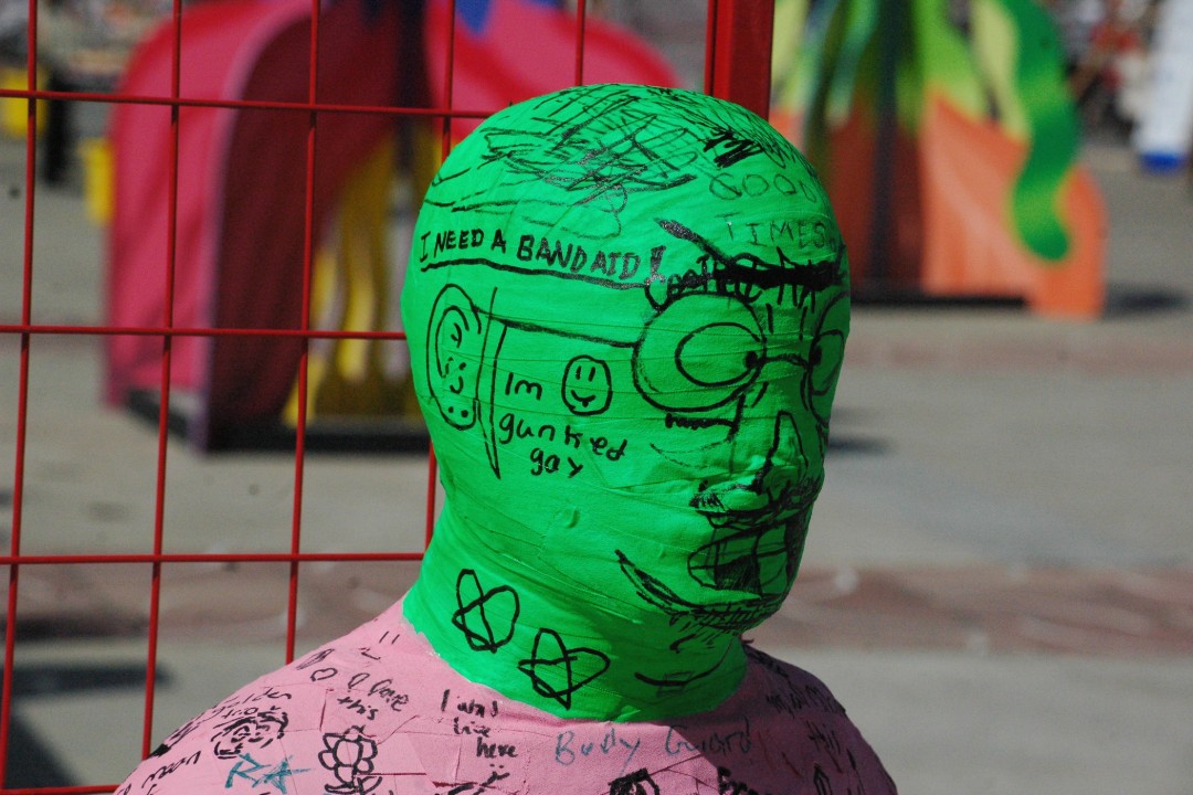 The head of a body-cast sculpture covered in tape, with words and drawing written on it. One message reads 'I need a Band-Aid.'