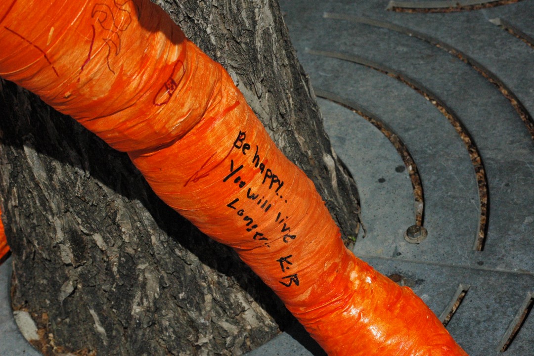 A closeup of a message written on a sculpture's tape-covered limb that reads 'Be happy... You will live longer'