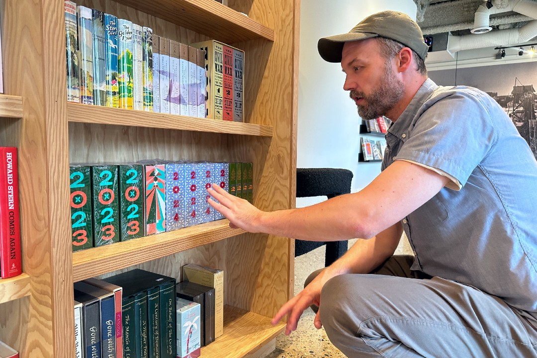 A man kneels next to a bookshelf with colourful books