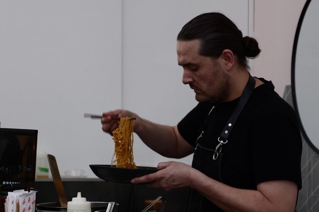 A chef using chop sticks to toss a noodle dish in a bowl