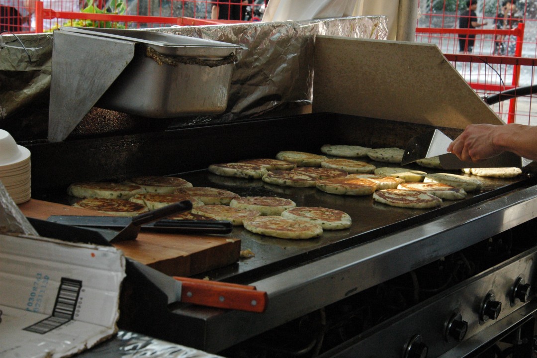 A cook tends to green onion cakes on a griddle in an outdoor booth