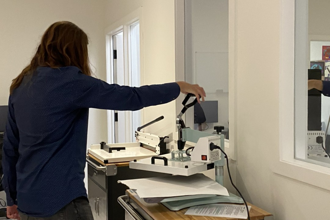 A person in a dark blue shirt operating a heat press that can press designs onto shirts