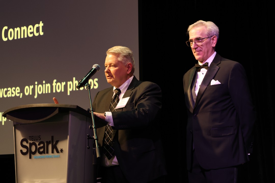 Two men in black-tie dress next to a podium on a stage with the word "Connect" displayed behind them