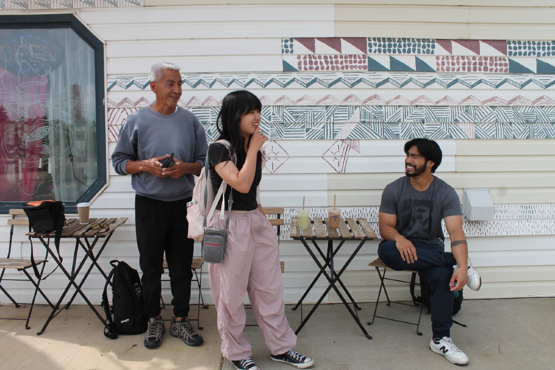 Three smiling people gathered in front a an outdoor mural
