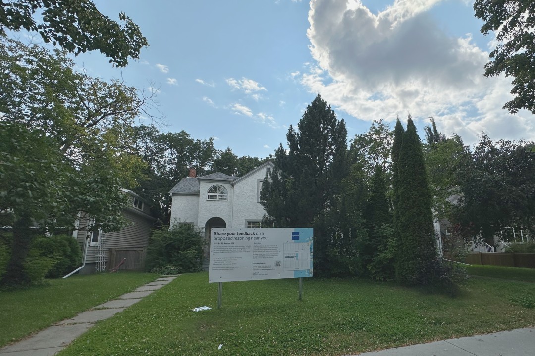 A white single-family house with a rezoning sign in front