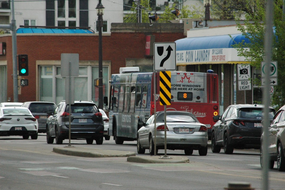 A bus surrounded by cars passes by a laundromat on 99 Street
