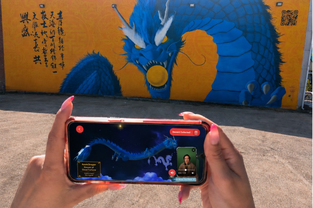 A mural of a dragon behind someone holding a phone with an alternate version of the dragon on the screen