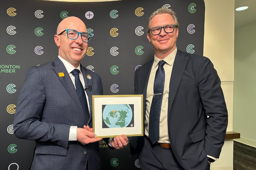 Two men in suits smile while holding a framed photo
