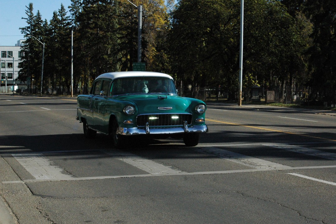 An old car with lots of chrome heads down a city street