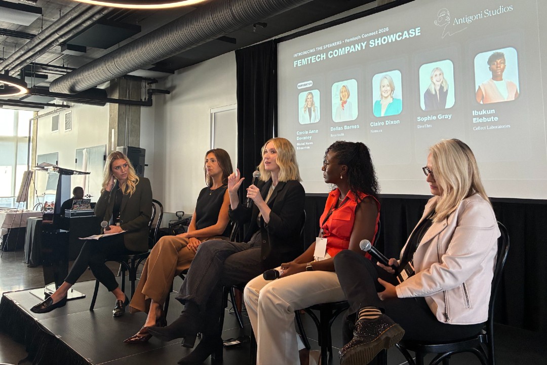 Five women seated on a stage with a projected image behind them that reads femtech company showcase