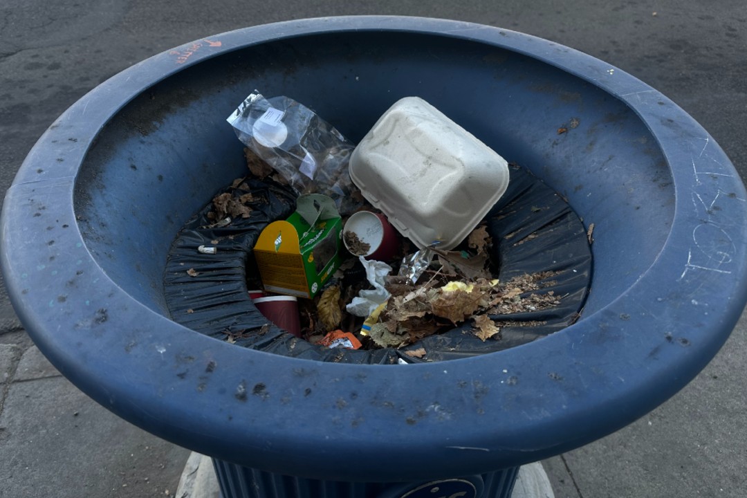 A paper takeout container among trash in a downtown garbage bin