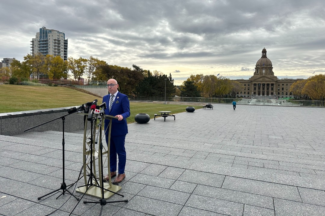 Mayor Andrew Knack stands in front of a podium with the Alberta legislature in the background