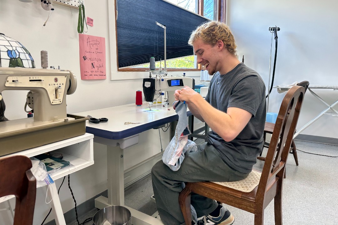 A person smiles while sewing jeans