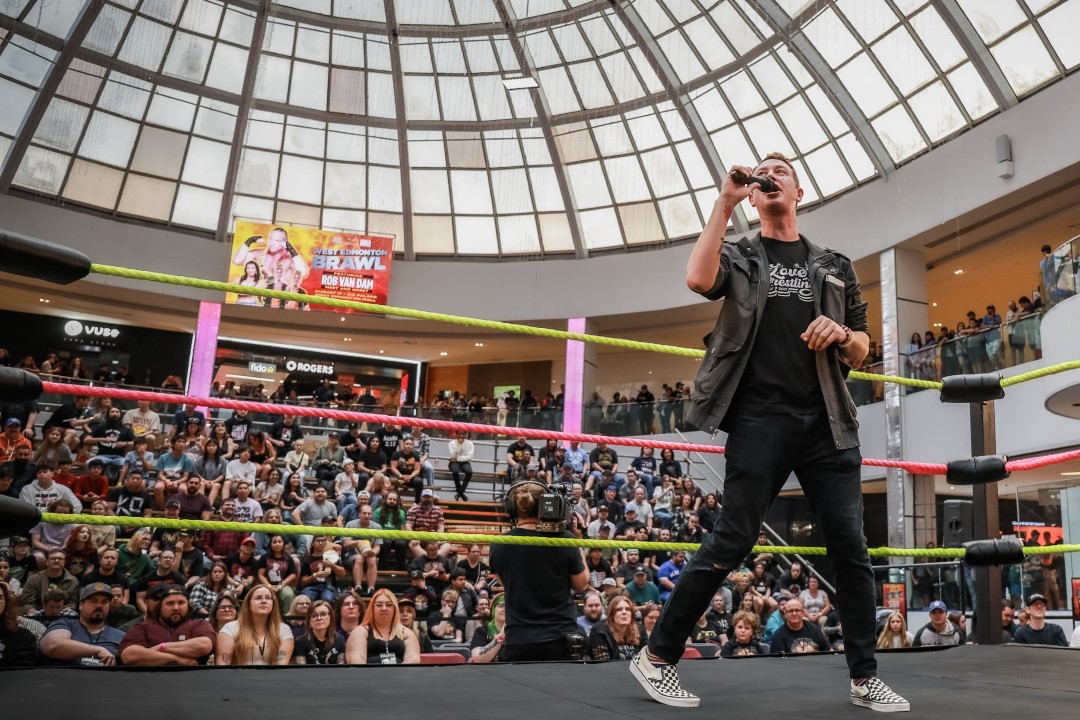 A man holding a microphone in a wrestling ring beneath a domed ceiling