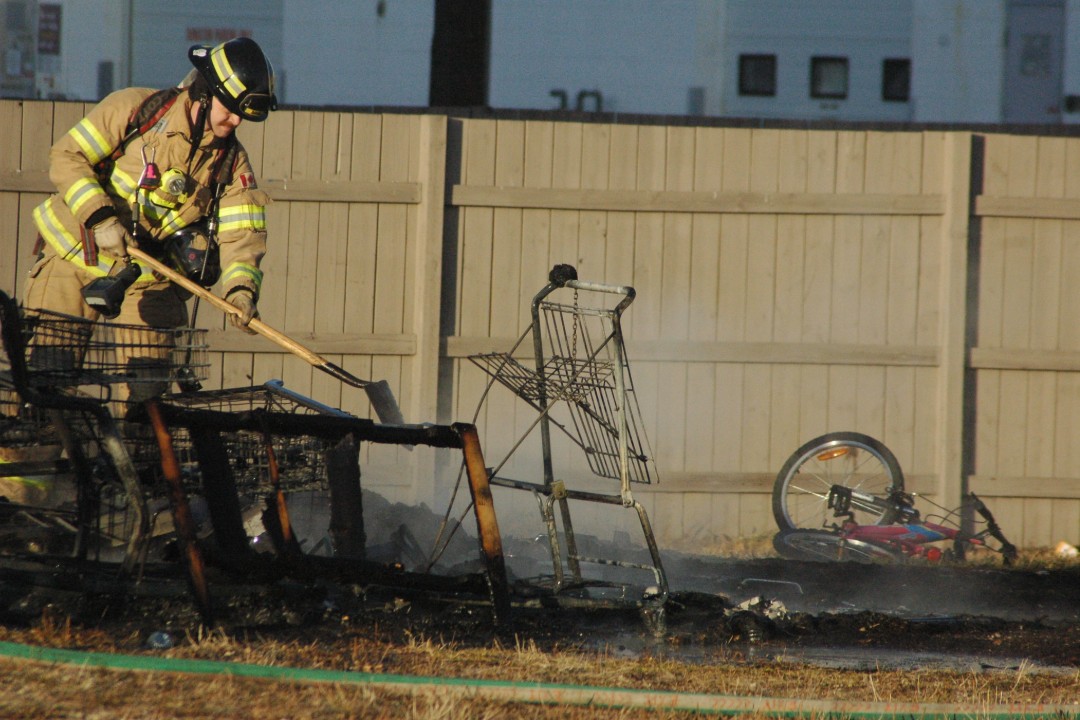 A firefighter wields a shovel beside burnt-out shopping carts