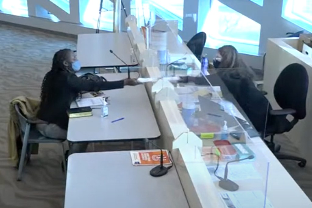 A screenshot from livestreamed video of a candidate and a clerk exchanging papers at City Hall.